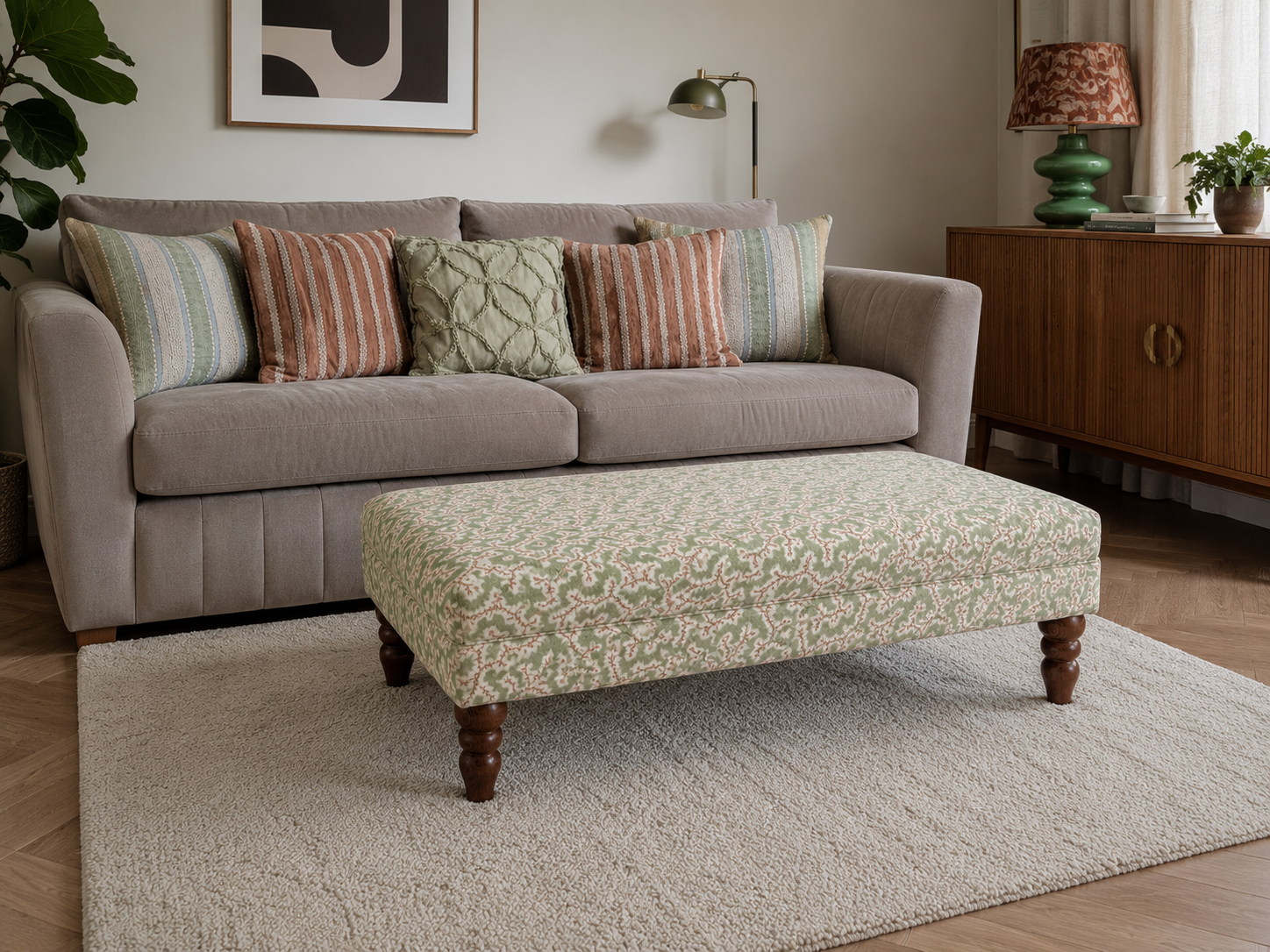 Modern stylish living room with an upholstered footstool in a green and pink botanical abstract swirl pattern on a cream rug.