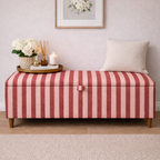 Striped ottoman with a pillow and small table in a room with a framed picture on the wall.