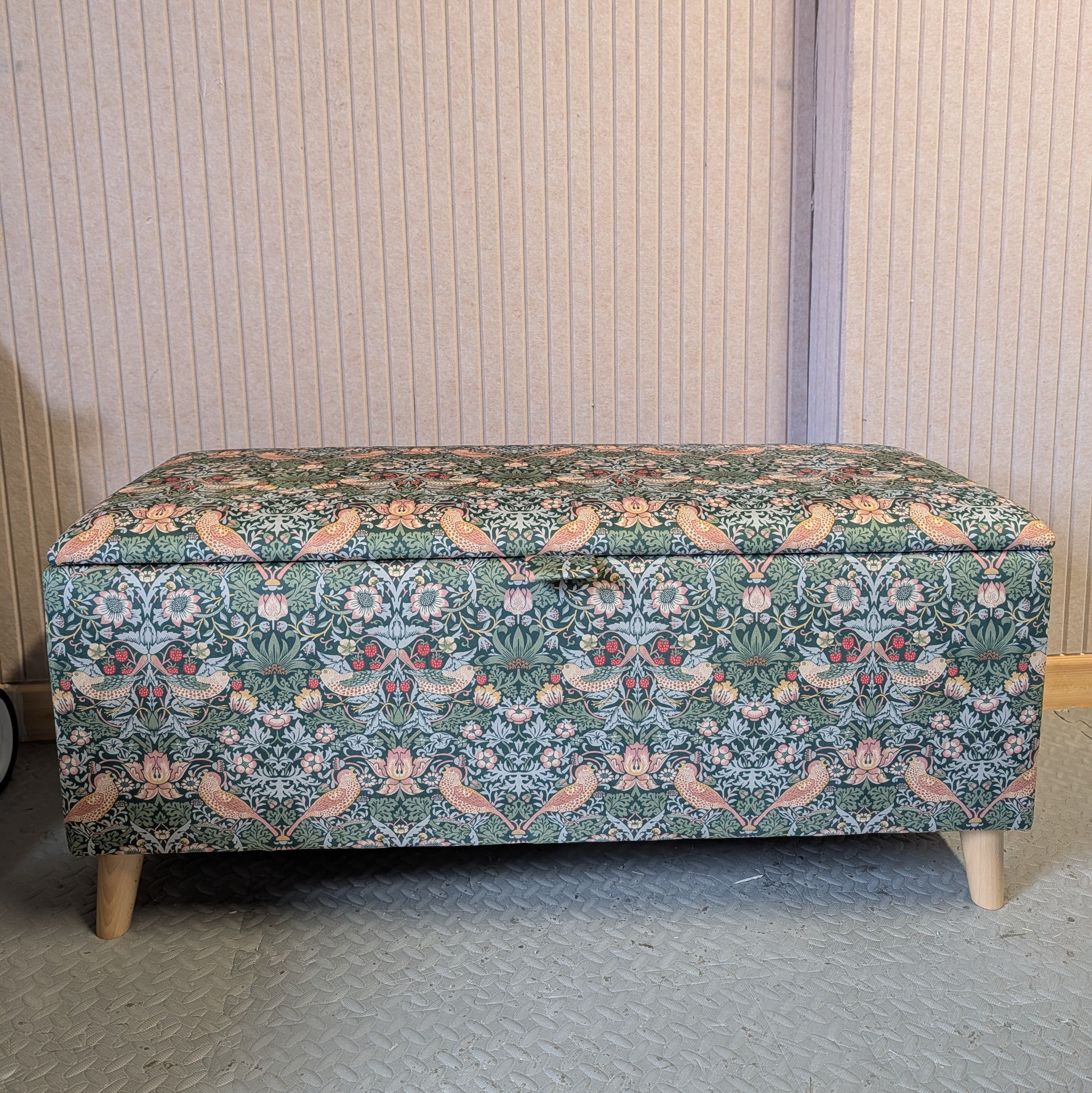 Floral William Morris patterned storage bench against a striped wall.