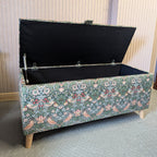 Floral-patterned storage bench with open lid in a room with wooden paneling.