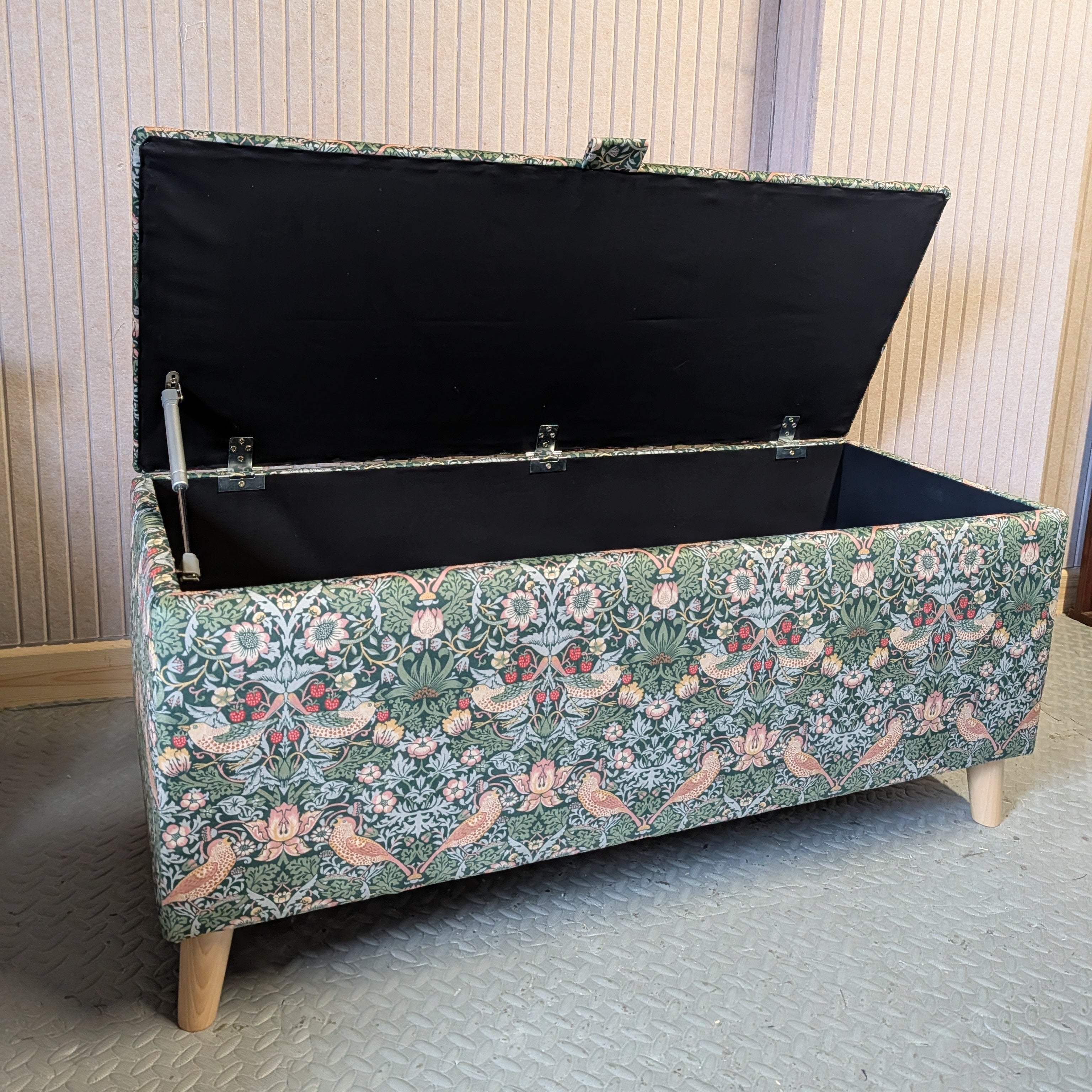 Floral-patterned storage bench with open lid in a room with wooden paneling.