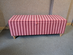 Pink striped storage bench on a gray floor with a wooden wall background