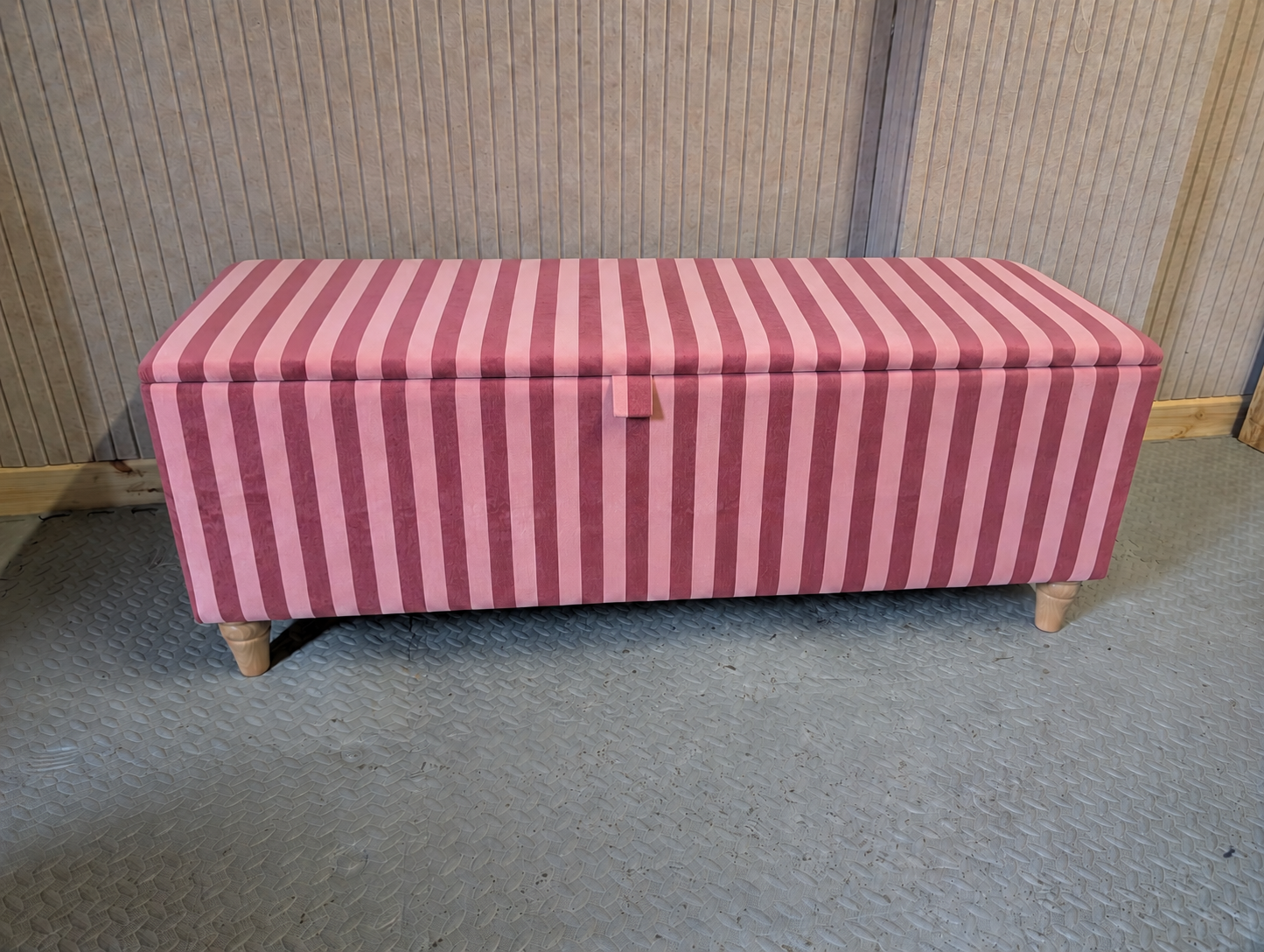 Pink striped storage bench on a gray floor with a wooden wall background