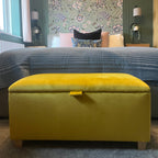 Yellow ottoman in a room with floral wallpaper and a window.