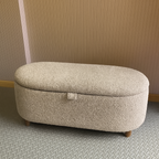 Beige ottoman with a textured bouclé surface on a patterned floor with slatted background wall.
