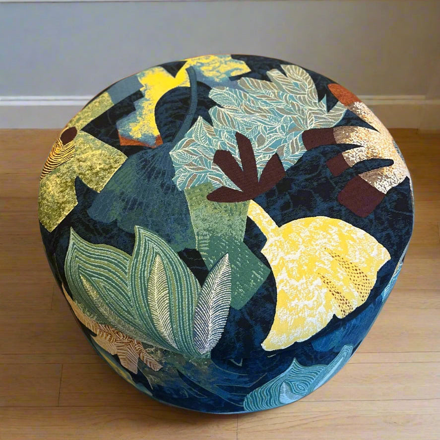 Round ottoman with colorful floral tropical pattern on wooden floor.