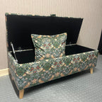 William morris forest green cushion inside a matching ottoman with black interior and angled wooden legs.