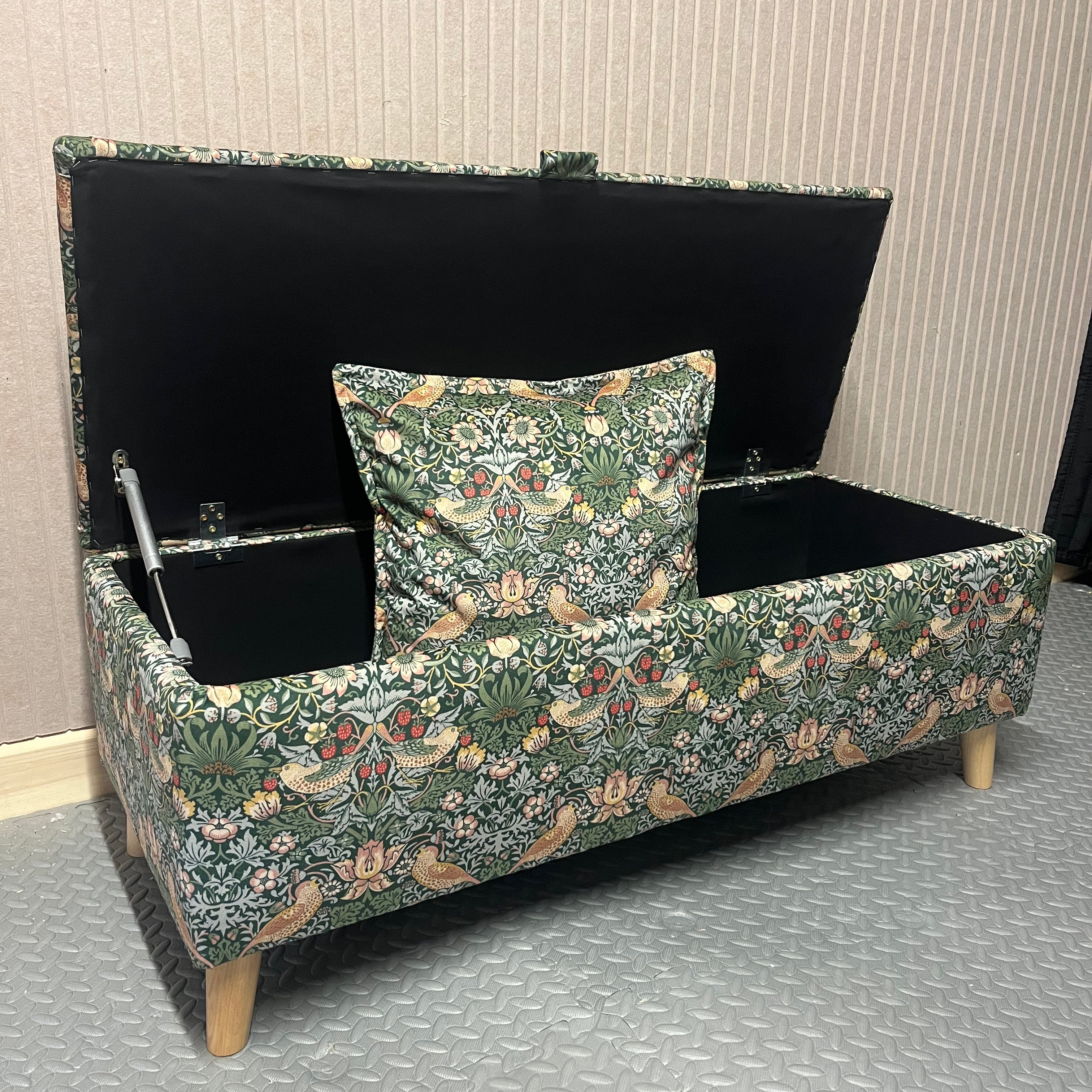 William morris forest green cushion inside a matching ottoman with black interior and angled wooden legs.