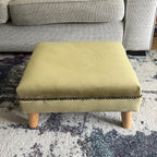Short and low olive green footstool in plush velvet with bronze trim and angled wooden feet