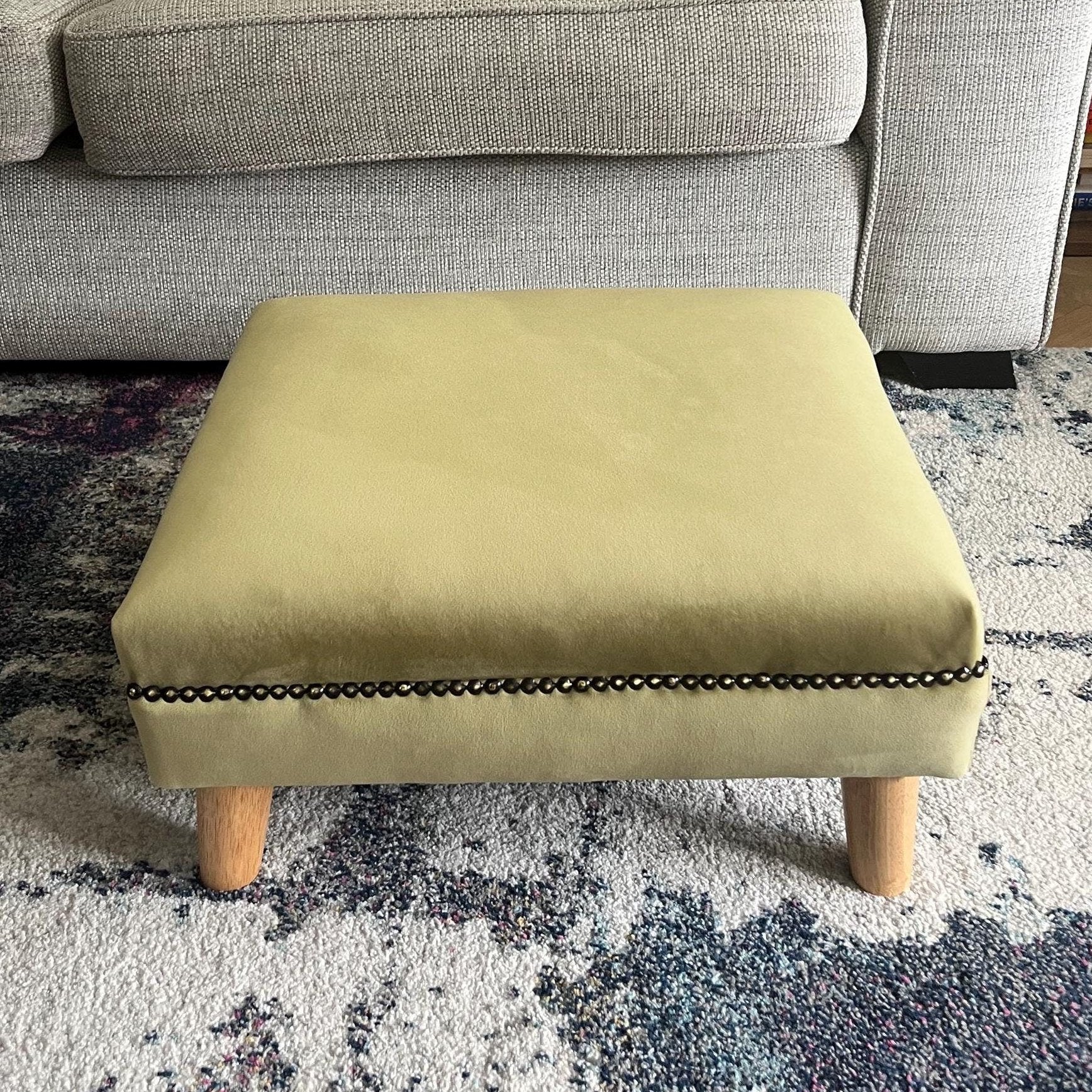Short and low olive green footstool in plush velvet with bronze trim and angled wooden feet
