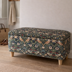 William morris ottoman on a wooden floor with a neutral rug and wall shelf in the background.